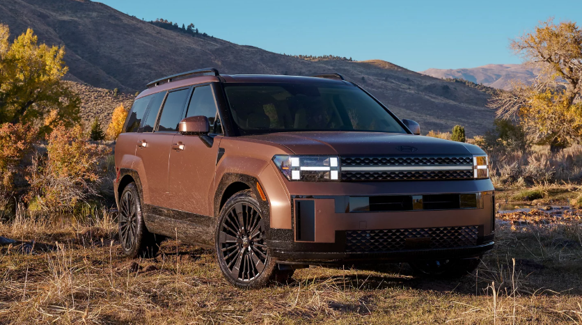 Bronze 2026 Hyundai Santa Fe Hybrid SUV parked outdoors with mountains in background.